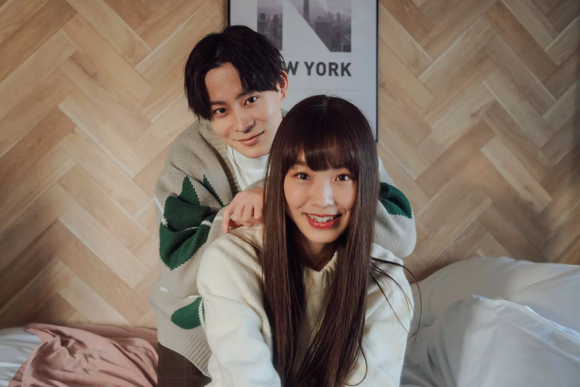 兩名使用者於室內空間合影，一人站在後方將手放在前方使用者肩上，兩人面向鏡頭微笑，背景為木質牆面與床鋪。